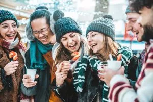 Amigos felices divirtiéndose bebiendo vino caliente y chocolate caliente en el Mercado de Navidad - Jóvenes alegres disfrutando de las vacaciones de invierno en las vacaciones de fin de semana - Enfoque en chico asiático