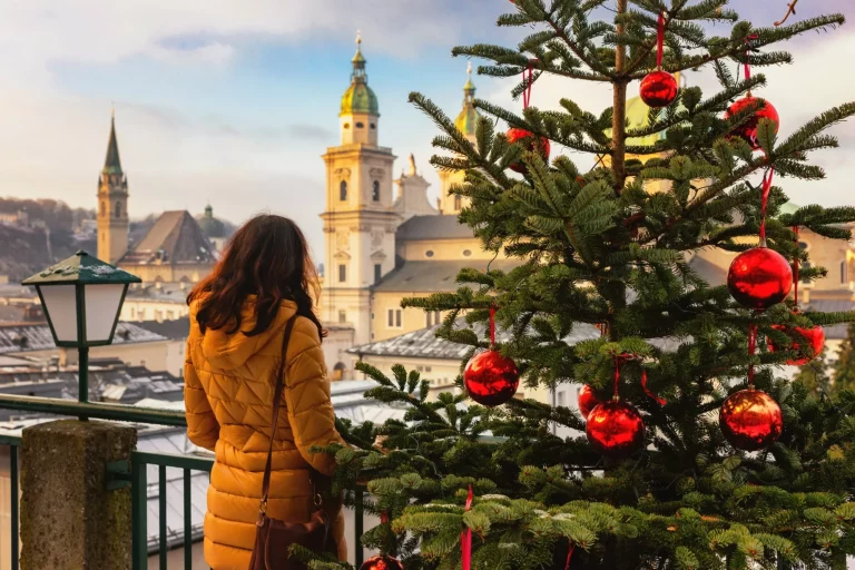Ung kvinne sett bakfra står på bakgrunn av solfylt jul i Salzburg, Østerrike. Juletrær med røde julekuler på bakgrunn av vinteren i Salzburg.