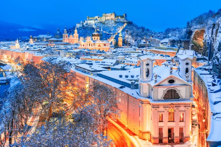 Salzburg, Österreich: Winterliche Ansicht der historischen Stadt Salzburg mit der berühmten Festung Hohensalzburg und der beleuchteten Salzach in wunderschöner Dämmerung während der malerischen Weihnachtszeit im Weinland