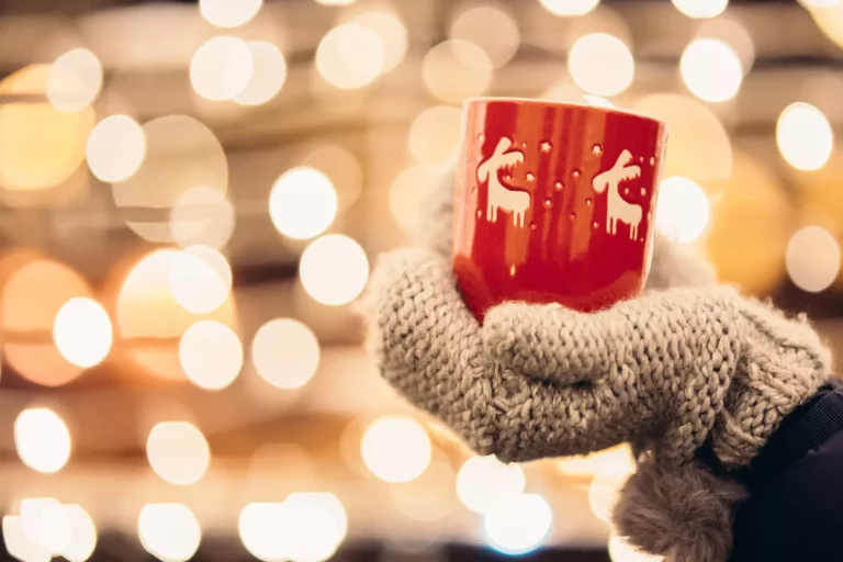 Julelys og en kvinne med et rødt krus med varm drikke i hånden